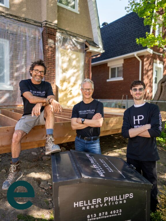 Three employees of Heller Philips Renovations stand around their branded bike trailer. 
